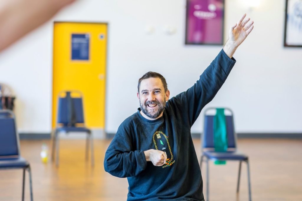 Happy bearded man doing indoor exercise, raising his arm enthusiastically.