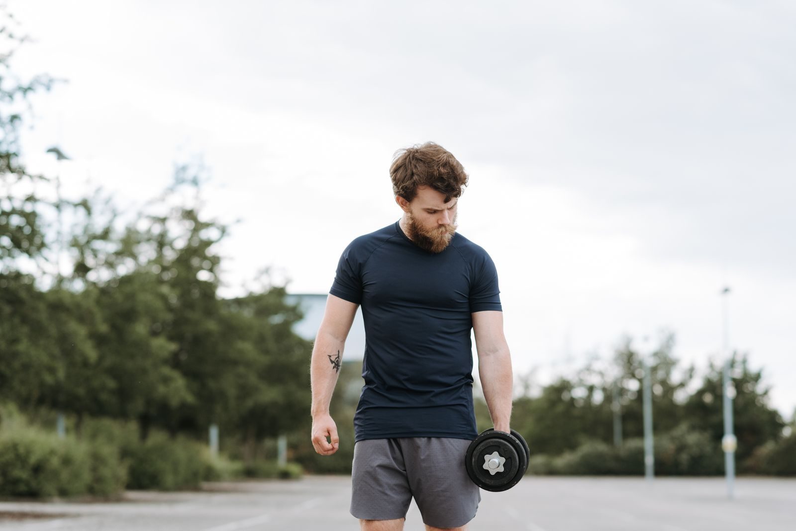 Serious sportsman looking down doing exercise with dumbbell while training on sports ground