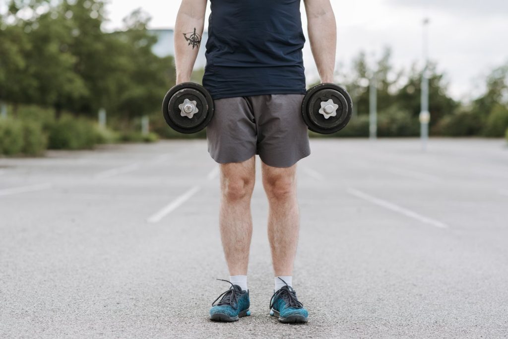 Crop unrecognizable male training with heavy dumbbells becoming stronger while working on body