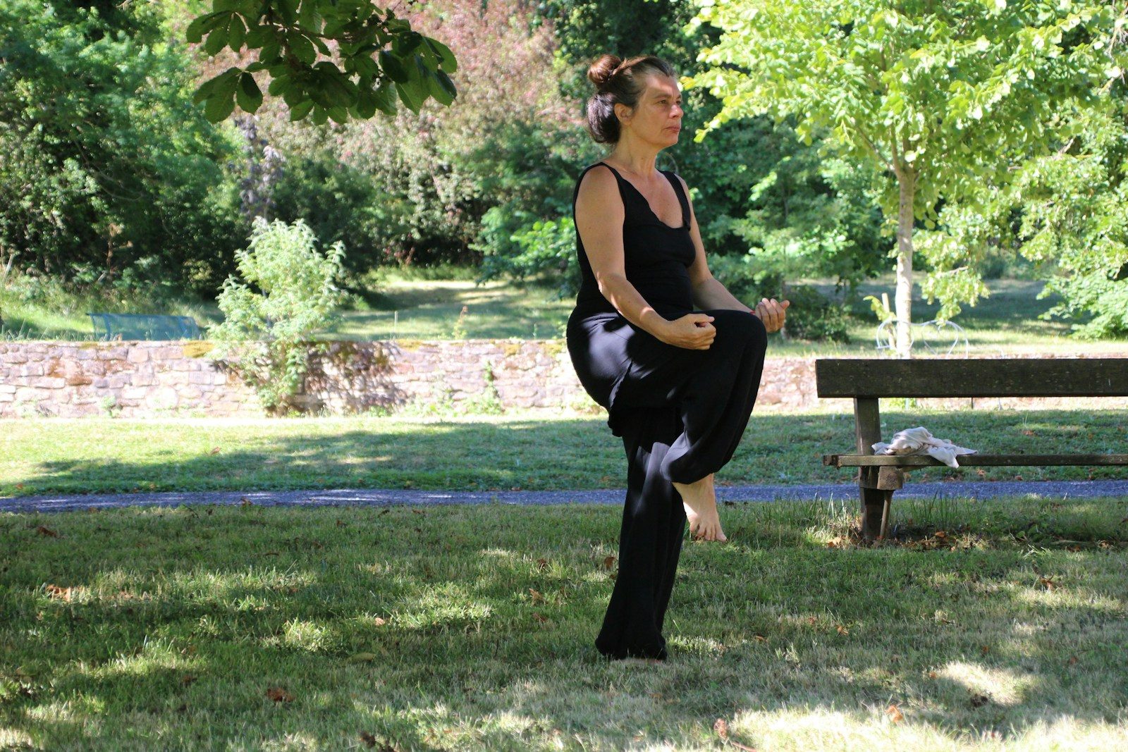 woman in black tank top and black pants sitting on brown wooden bench under green tree
