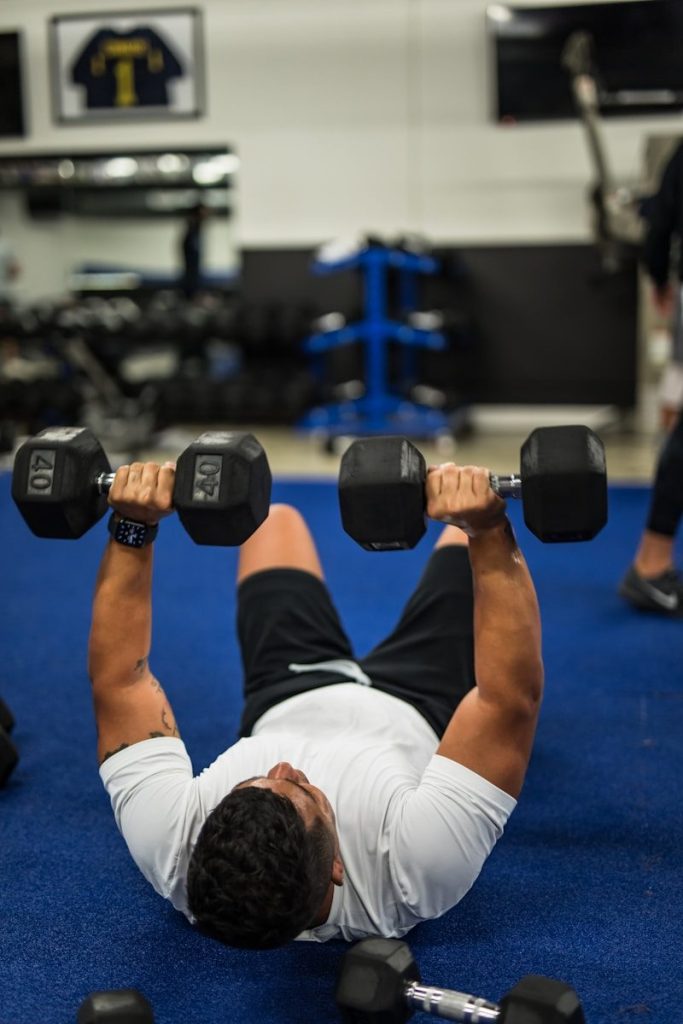 man in white tank top and white shorts holding black dumbbell