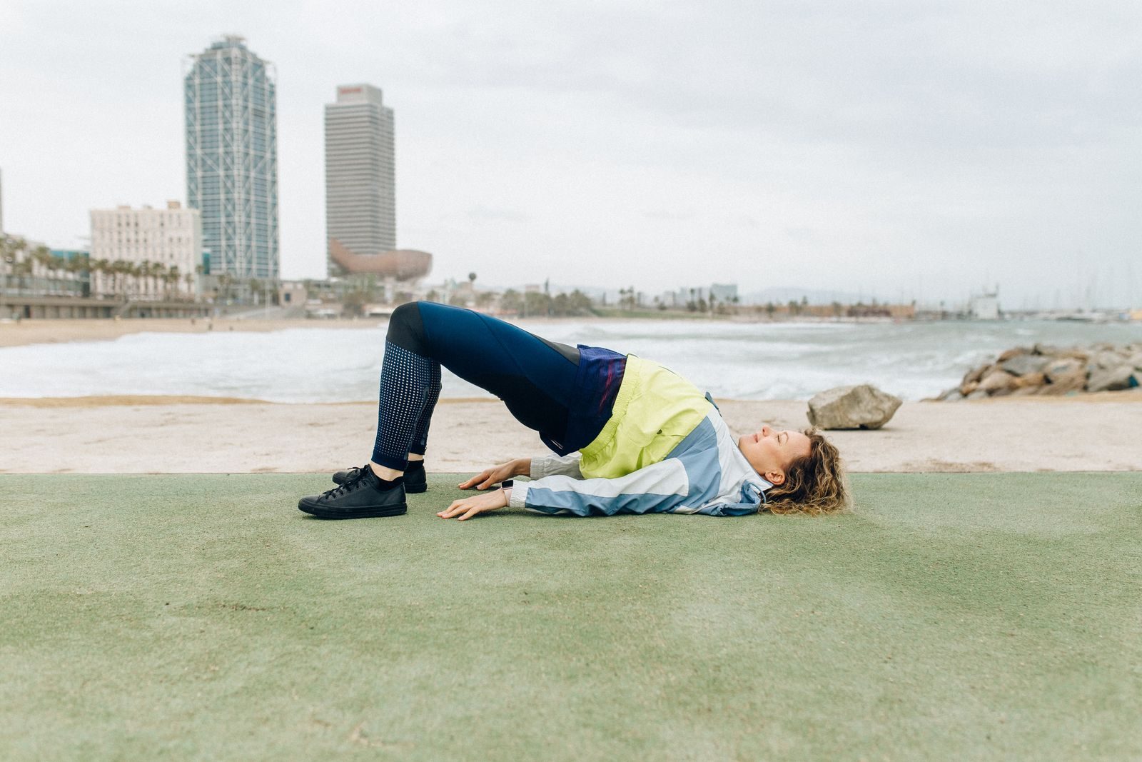 A woman in activewear exercises near the beach with skyscrapers in the background, embodying a healthy lifestyle.