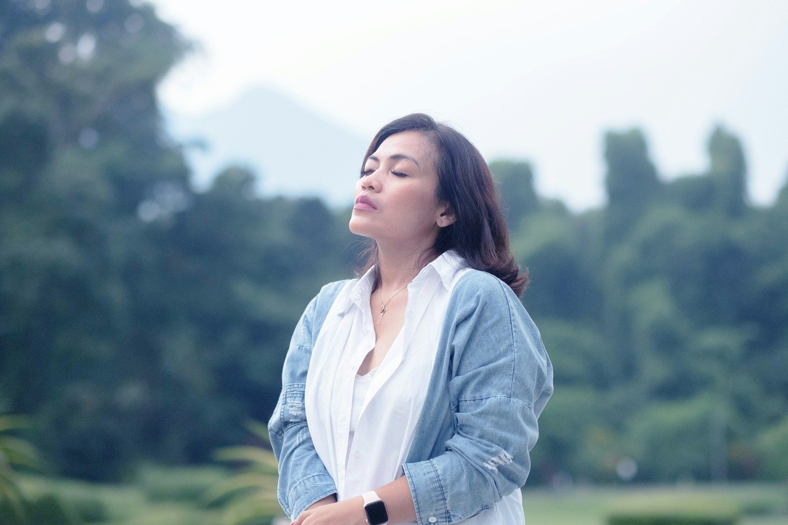 a woman standing in a park with trees in the background