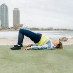 A woman in activewear exercises near the beach with skyscrapers in the background, embodying a healthy lifestyle.