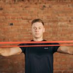 Adult male using a resistance band for fitness training against a brick wall backdrop.