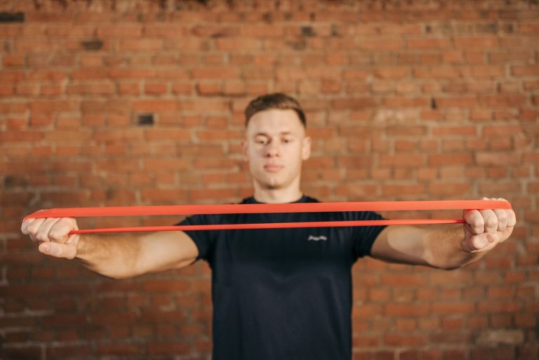 Adult male using a resistance band for fitness training against a brick wall backdrop.
