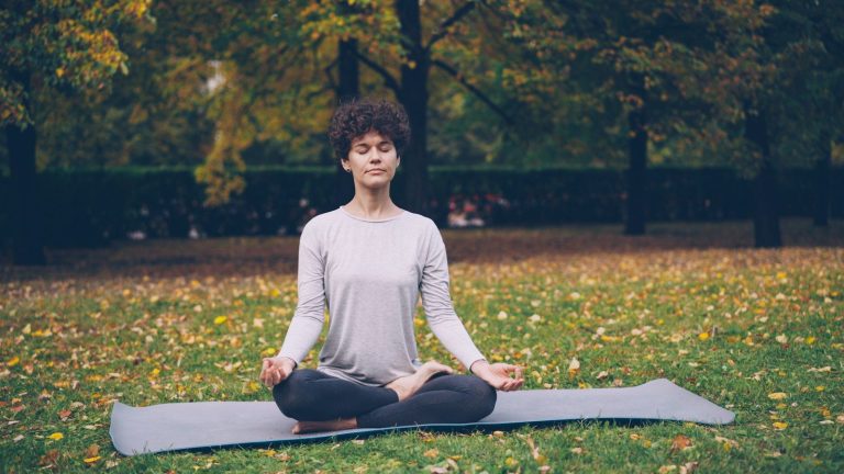 Woman meditating peacefully on a yoga mat outdoors